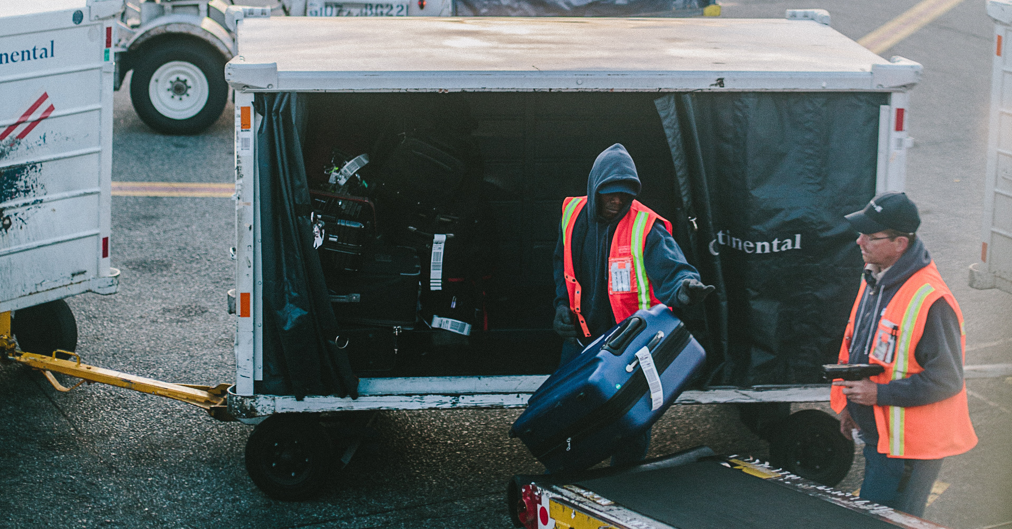 two baggage handlers move bags from a cart to a conveyor belt